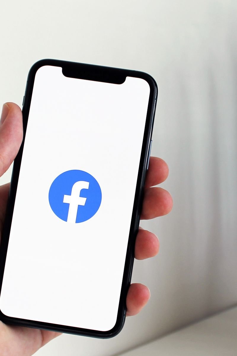 Close-up of a hand holding a smartphone displaying the Facebook logo indoors.